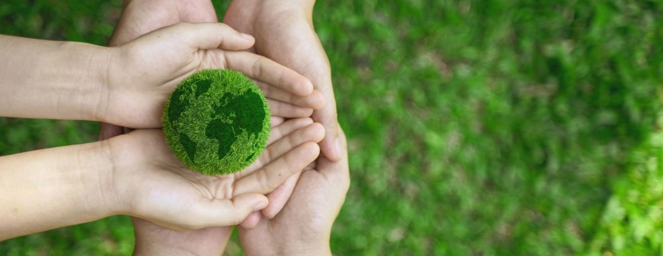 Hands holding a small green globe made of grass, symbolizing environmental sustainability