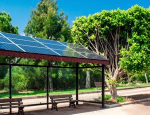 Bus stop shelter fitted with rooftop solar panels, surrounded by trees and greenery on a sunny day