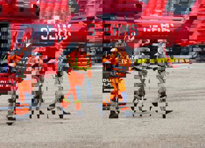 Air ambulance crew in orange flight suits walking away from a red helicopter during an emergency response