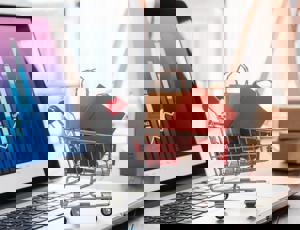 Small shopping trolley graphic filled with packages placed on a laptop displaying data charts