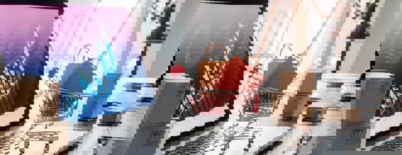 Small shopping trolley graphic filled with packages placed on a laptop displaying data charts