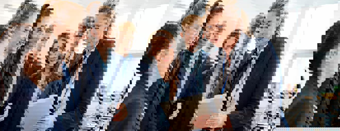 Group of students gathered around another person holding a tablet during a lab activity