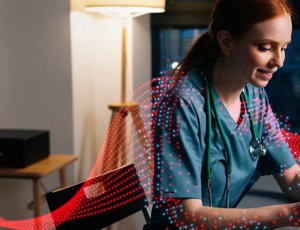 Healthcare professional in scrubs working on a laptop at a desk with digital wave graphics overlayed