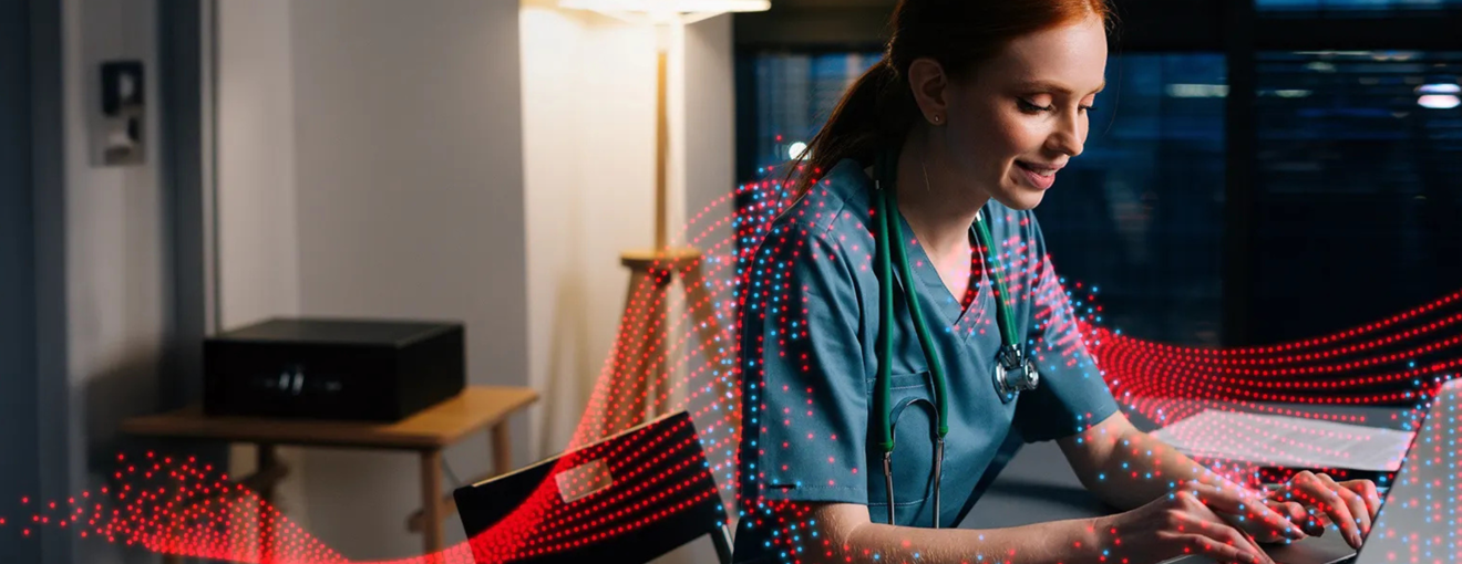 Healthcare professional in scrubs working on a laptop at a desk with digital wave graphics overlayed