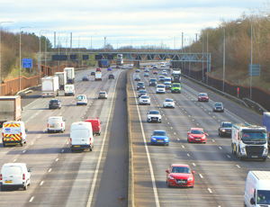 Busy multi‑lane motorway with cars, vans, and lorries travelling in both directions on a clear day