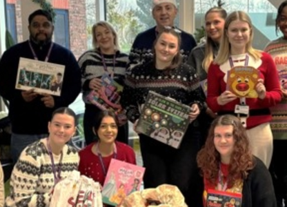 Procurement services team in festive jumpers holding christmas donations 