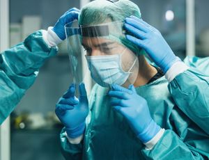 Medical staff wearing protective gowns, gloves, and face shields helping a colleague adjust their protective equipment