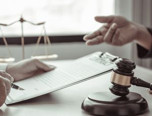 Lawyer reviewing and signing documents on a clipboard as another person gestures during a legal consultation