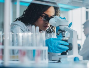 Scientist wearing gloves using a microscope in a laboratory with test tubes and equipment in the foreground